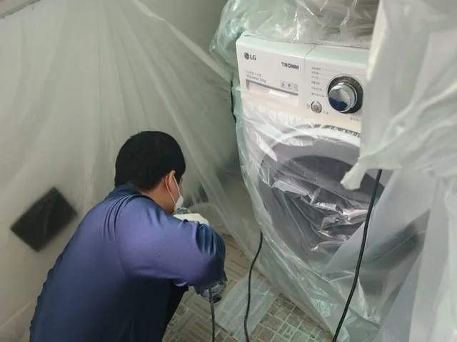 세탁기와 벽에 비닐을 두르고 바닥을 작업하는 모습